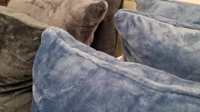 Soft plush decorative pillows in blue and gray colors displayed on a shelf in a retail store. Home decor textile, interior styling decoration, cozy household items shop.