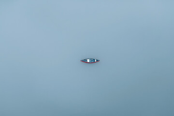 Minimalist aerial view of a small red wooden canoe floating on calm blue water © Feeney