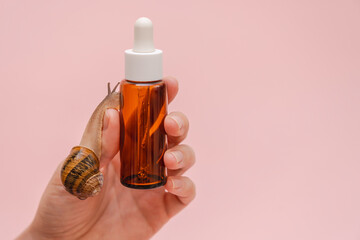 Woman's hand holding glass cosmetic bottle with snail. Mockup for your brand. Skin care product, spa, luxury, natural beauty © Antonio