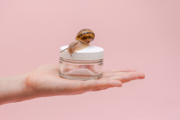 Glass cosmetics bottle with snail in woman's hand. Mockup for brand. Skin care product, spa, luxury, natural beauty cream © Antonio