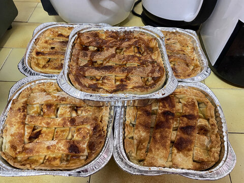 Freshly baked homemade apple pie in aluminum trays, featuring golden flaky crust and a warm caramelized apple filling prepared in a home kitchen.