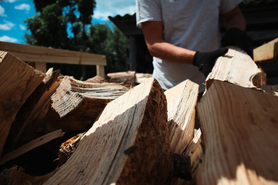 Man wearing protective gloves stacking split wooden logs onto rack preparing firewood in backyard