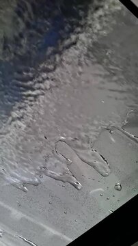 View from inside car during automatic robot car wash with water drops flowing on glass and foam covering window. 