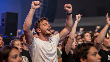 Fototapeta premium Enthusiastic crowd cheering with raised fists at live concert event under stage lights.