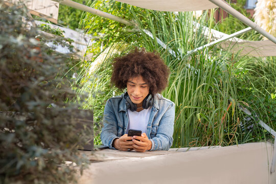 Smiling young ethnic guy 20 years old, dressed in casual clothes, works on a laptop outdoors, in a green area in nature. Green open space for coworking, freelancer, relaxing, coffee, food. Free place 