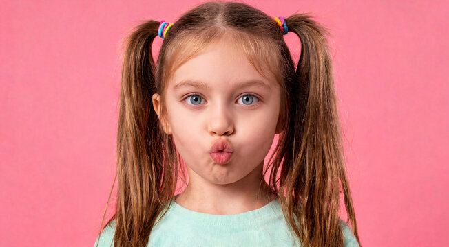 Child makes a funny face with pouted lips against a pink background in a playful moment at home