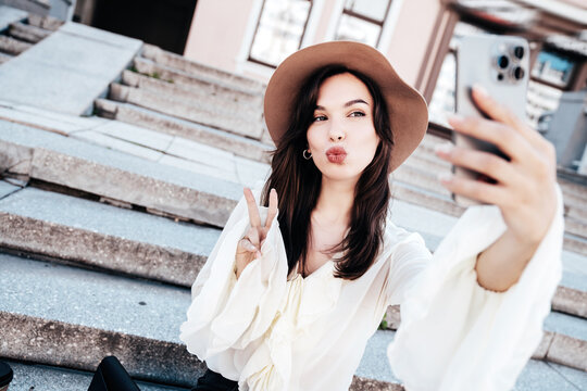 Portrait of young beautiful smiling hipster woman in trendy summer white blouse and jeans. Carefree woman posing in the street in sunny day. Positive model outdoors. Cheerful and happy. take selfie