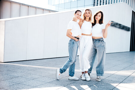 Three young beautiful smiling hipster female in trendy summer white t-shirt  and jeans clothes. Sexy carefree women posing in street. Positive models having fun, going crazy. In sunny day