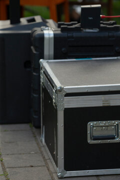 Stacked equipment cases in backstage loading scene with metal corners and recessed handles, flight cases and generator in background, overcast