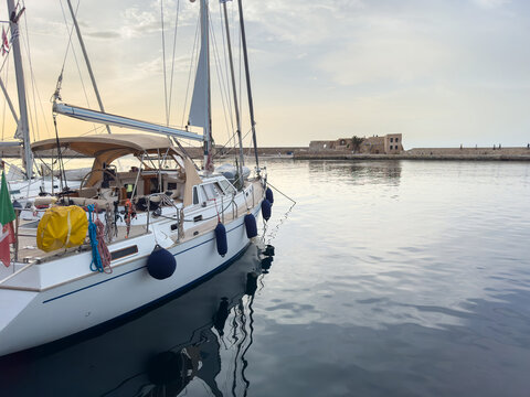 White sailboat on calm water in Chania Old Harbor, Crete, Greece, hazy evening