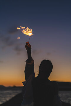 夕暮れの海で花火をする女性