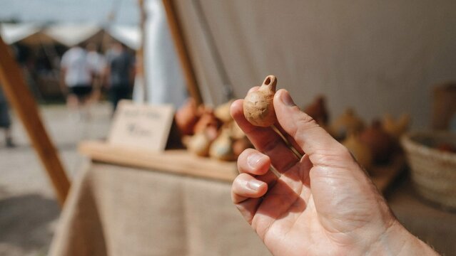 Person holding a small handmade clay whistle at an outdoor artisan craft market stall with holds small unglazed