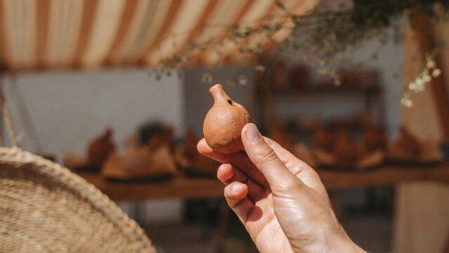 Hand holding small clay whistle in pottery workshop with holding brown ceramic whistle craft studio handmade