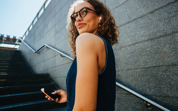 Young woman ascends stairs holding a smartphone during city commute