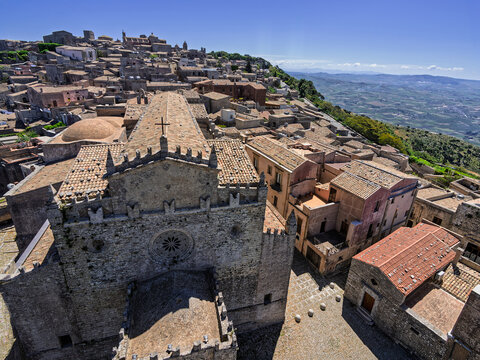 High-angle panoramic view from King Frederick's Tower over the Real Chiesa Madrice, medieval Erice rooftops, and the sweeping Val di Mazara plains in Sicily.