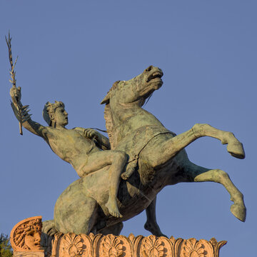 A detailed low-angle shot of the bronze equestrian statue by Benedetto Civiletti crowning the roof of Teatro Politeama Garibaldi against a clear blue sky in Palermo.