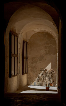 Traditional stone archway and entrance hallway featuring old wooden shutters and natural shadows in Siracusa, Italy. Scenic Mediterranean building interior view.
