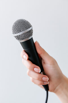 A hand holds a black microphone with a silver grille against a light background.