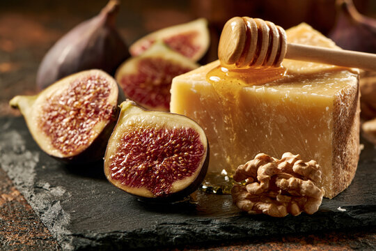 A slate cutting board featuring pecorino or feta cheese, fresh figs cut open, a handful of walnuts, and a  honey dipper.