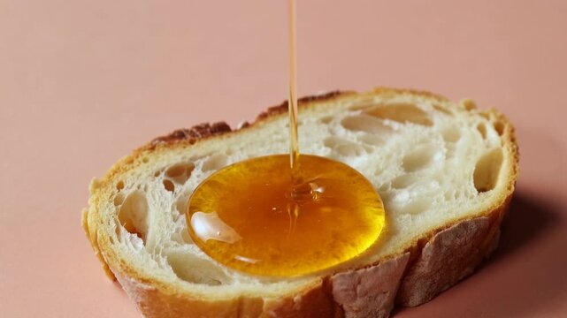 Lifting honey dipper pouring golden honey onto crusty bread on pink tabletop, for food styling