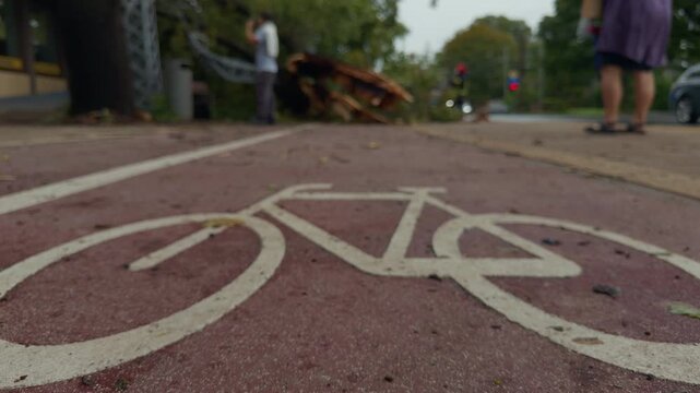 Low angle view of bicycle lane marking on urban street with blurred pedestrians and passing car