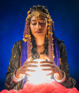 A fortune teller holds a glowing crystal ball with eyes closed