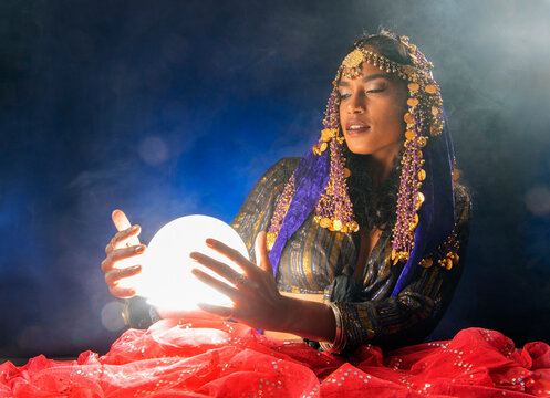 A South Asian woman dressed as a mystical figure holds a glowing