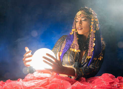 A fortune teller South Asian woman holds a glowing crystal ball