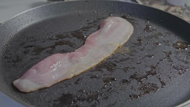 Loncha de bacon fresco fri&eacute;ndose en una sarten en su propia grasa