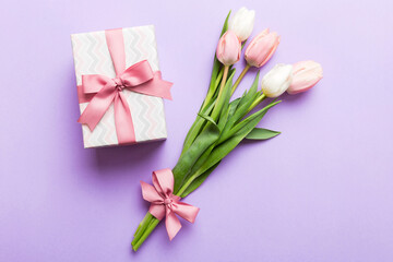 Naklejka premium Pink tulips flowers and gift or present box on colored table background. Mothers Day, Birthday, Womens Day, celebration concept. Space for text top view