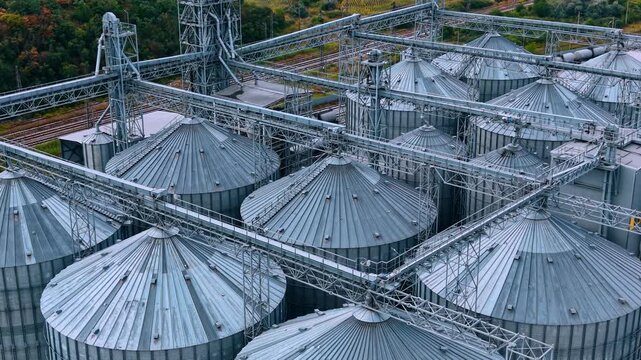 Aerial view of steel silo roofs and trusses. Metal framework spans over circular storage bins near railway tracks in daylight.