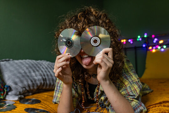 Teenage girl covers her eyes with CDs and sticks her tongue out