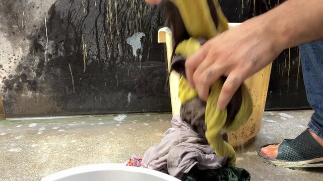 Adult man crouching outdoors washing clothes by hand in a plastic bucket