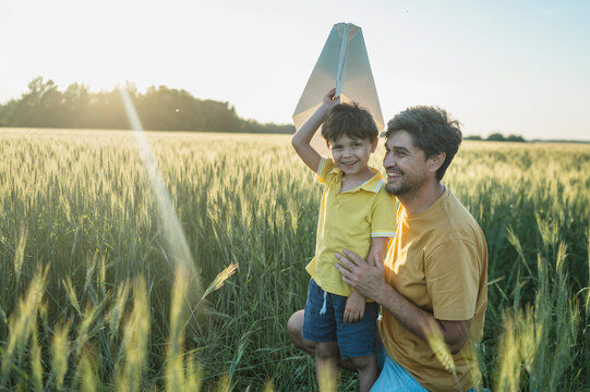 Father and son launch a paper airplane in a summer wheat field