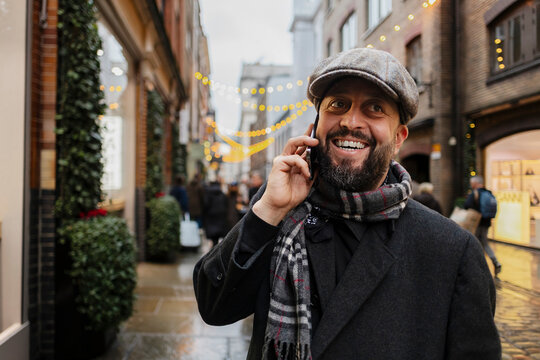 Smiling man with beard talking on smartphone in festive winter street