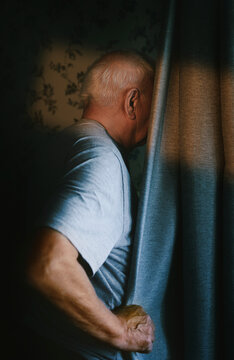 A man hides behind a curtain indoors at sunset