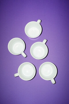 Empty white porcelain coffee cup arrangement on purple background