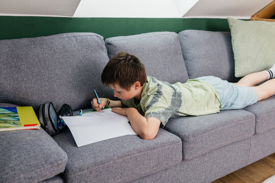 Student lying on sofa doing homework at home