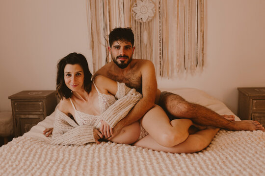Pregnant woman and man embrace on a bed in a cozy bedroom