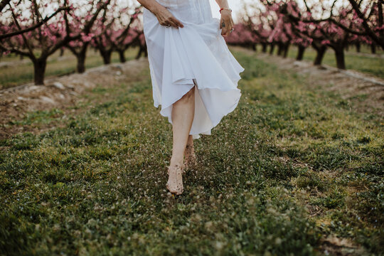 Woman wears a white dress and walks barefoot in a spring orchard