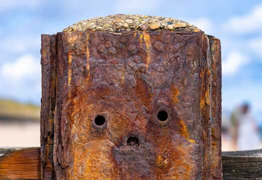Close-up of a heavily rusted steel coastal groyne at Waxham Beach, Norfolk, England. Corrosion, holes and weathered metal create a distinctive face-like appearance.