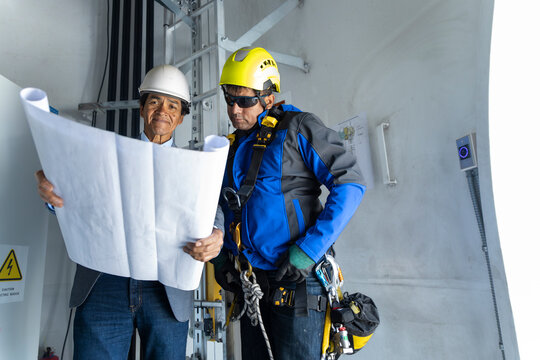 Coworkers examine a project blueprint inside a wind turbine
