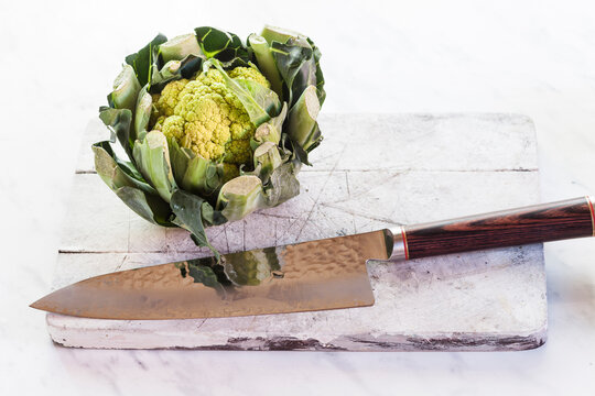 Green cauliflower and knife on chopping board