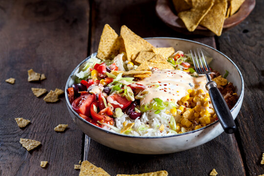 Taco salad bowl with rice, corn, chili con carne, kidney beans, iceberg lettuce, sour cream, nacho chips, tomatoes