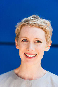 Portrait of smiling blond woman in front of blue background