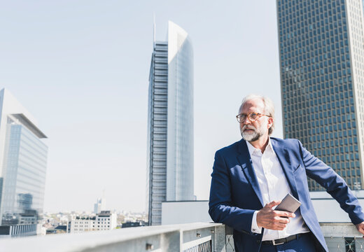 Mature businessman with cell phone in the city looking around