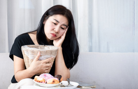Asian woman feeling nauseous holding trash bin. Perfect for morning sickness, food poisoning, indigestion, unhealthy diet, and vomit concept