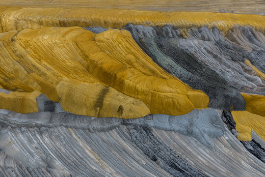 Aerial view of the textured landscape of the Tagebau Hambach open-pit mine, showing layers of yellow sand and grey coal deposits in Elsdorf, Nordrhein-Westfalen, Germany.