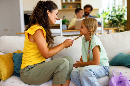 Mother gently arranging her daughter&rsquo;s braid while they sit together on a sofa at home