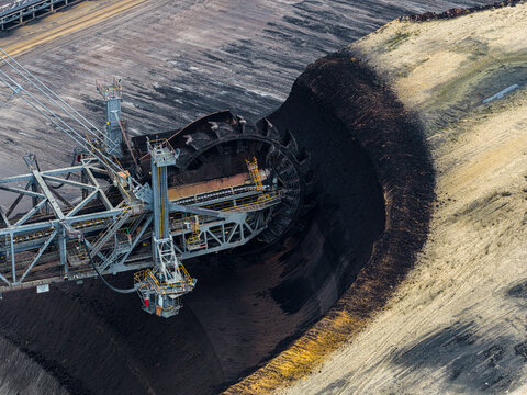 Aerial view of a bucket-wheel excavator at the Garzweiler surface mine, showing the deep excavation site with dark earth and steep slopes in Juchen, North Rhine-Westphalia, Germany.